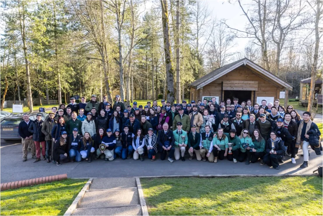 A large group photo of shooters from several universities outside a lodge