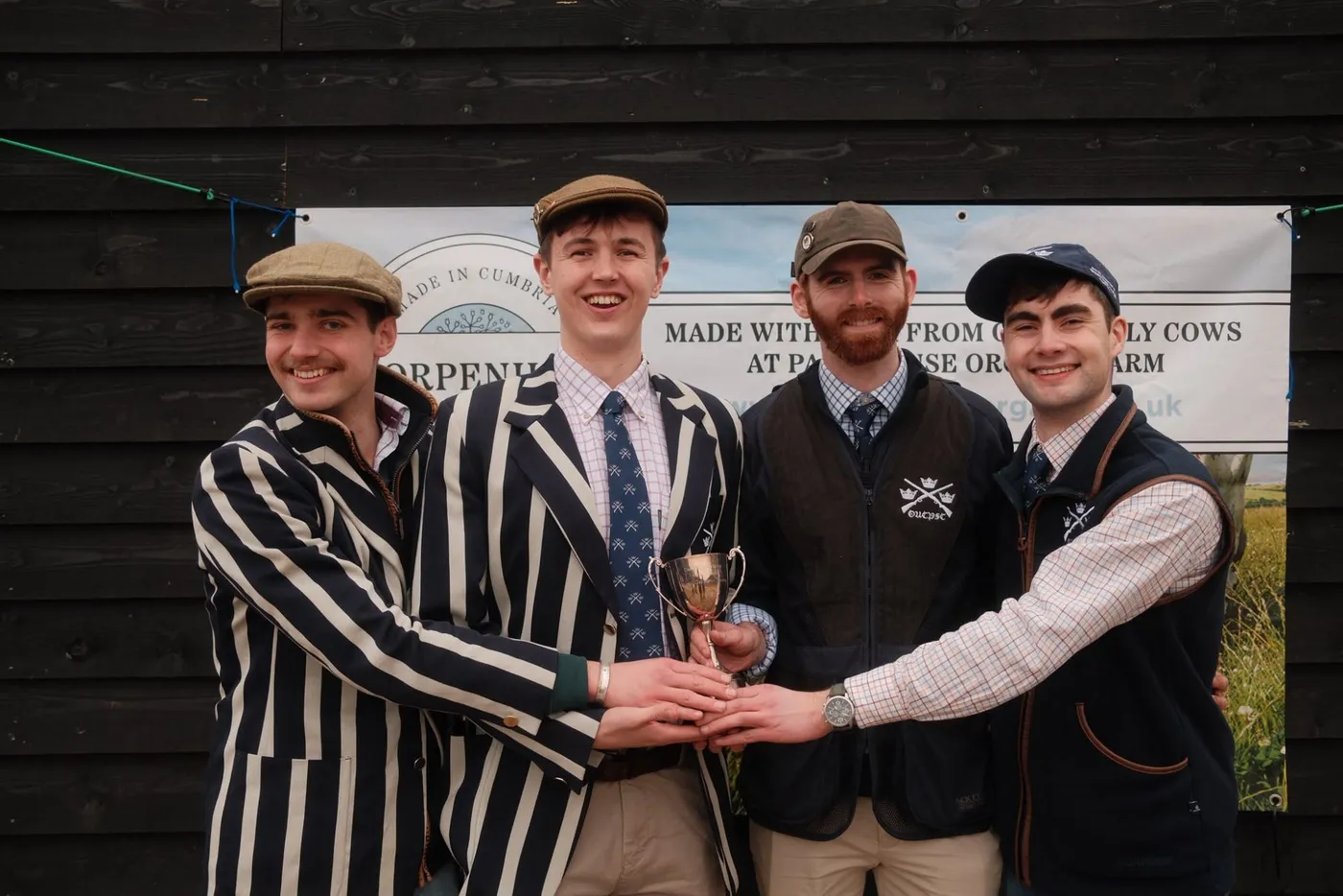 Four members in club blazers and gilets holding a cup
