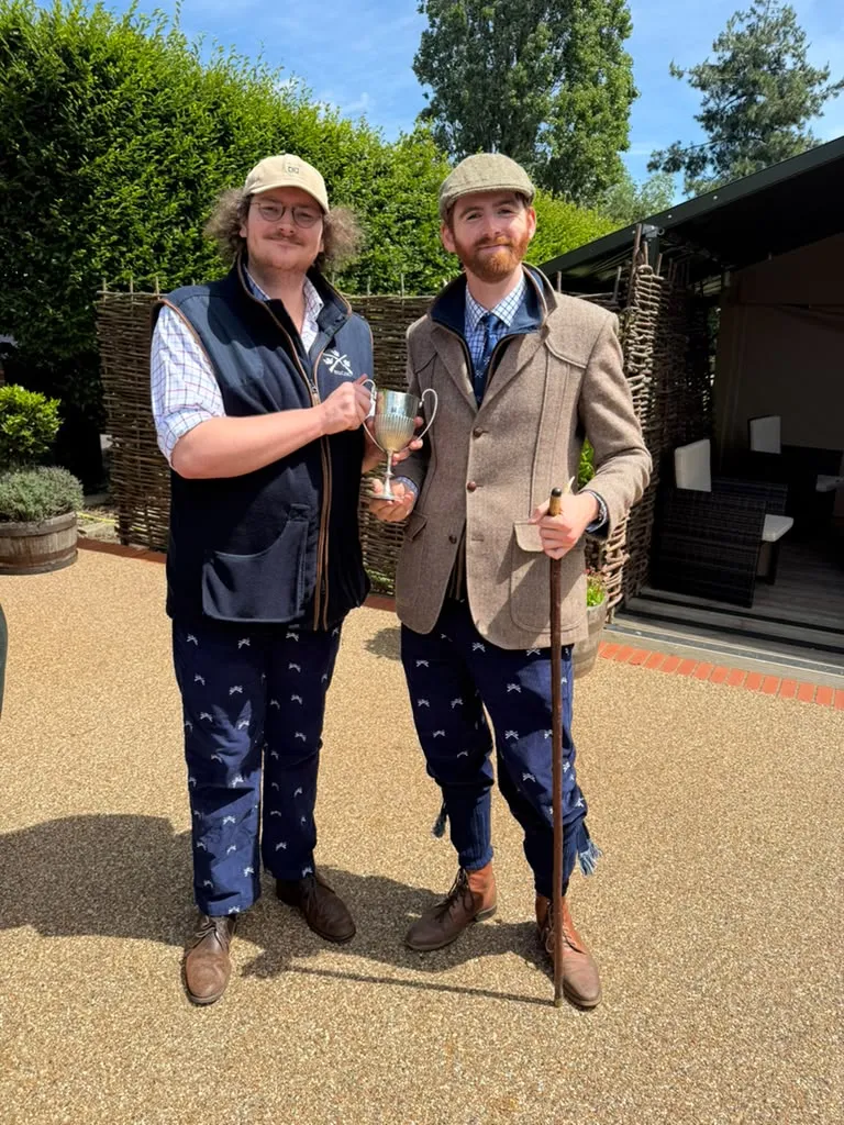Two members in club gilets and breeks holding a cup